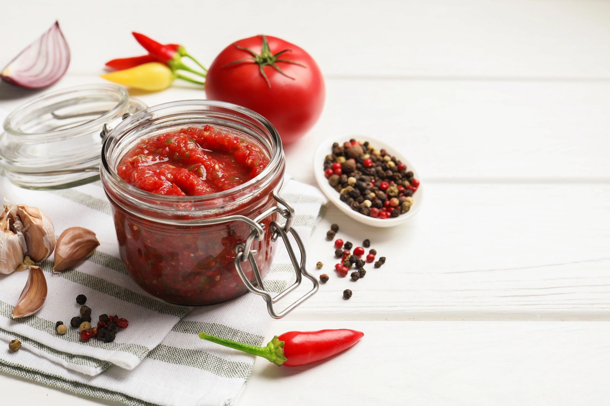 Tasty salsa sauce in jar and ingredients on white wooden table, closeup. Space for text
